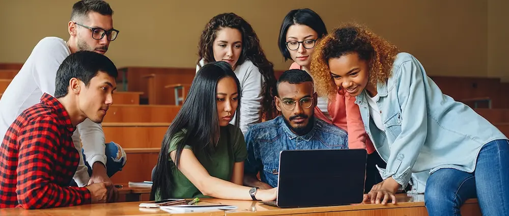 College students collaborating around a laptop in a lecture hall