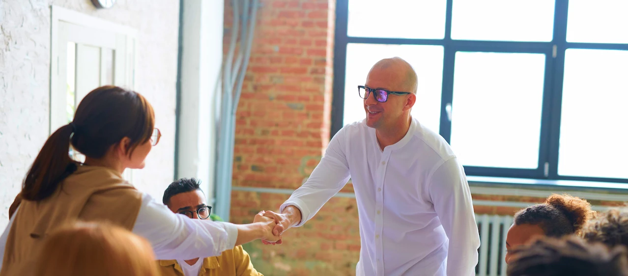 Business professionals shaking hands during a team meeting in a bright, modern office.